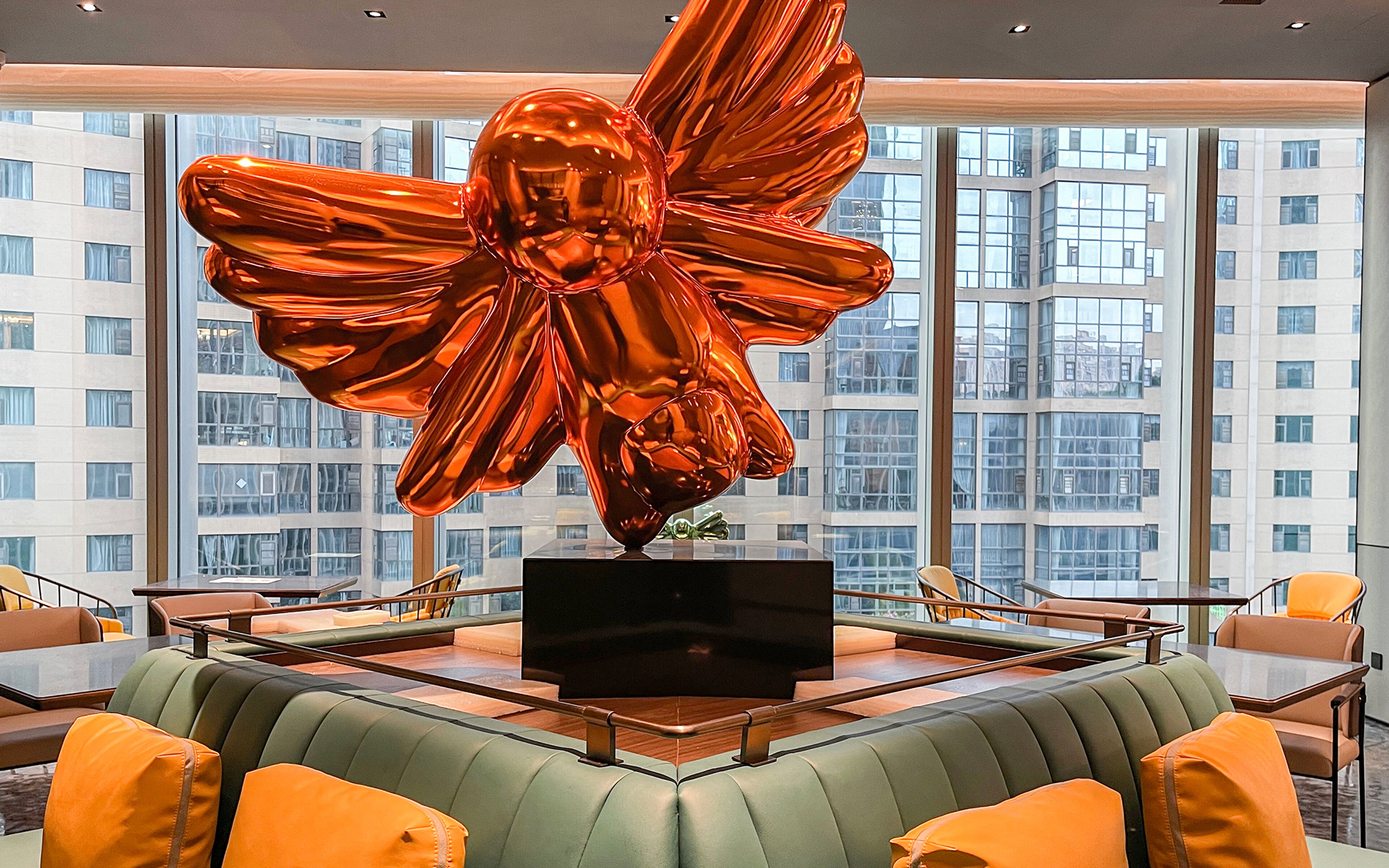 A modern interior with a large metallic sculpture, a flat-screen TV on a central table, and a seating area with cushioned chairs and sofas.