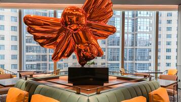 A modern interior with a large metallic sculpture, a flat-screen TV on a central table, and a seating area with cushioned chairs and sofas.
