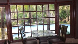 A dining area with a glass table and chairs, large windows with a view of a pool and palm trees. - Citrus Hotels Sriperumbudur (Sriperumbudur)