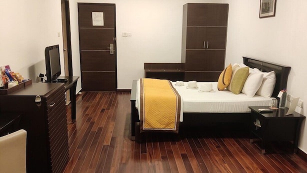 A hotel room with a bed, a desk, a chair, a wardrobe, and a television. - Citrus Hotels Sriperumbudur (Sriperumbudur)