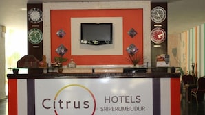 A hotel reception desk with a sign reading "Citrus Hotels" and a television screen above it. - Citrus Hotels Sriperumbudur (Sriperumbudur)