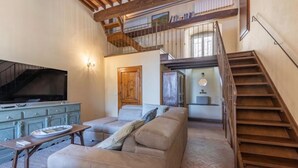 A spacious living area with a sofa, a coffee table, and a TV. There is a staircase leading to an upper level.