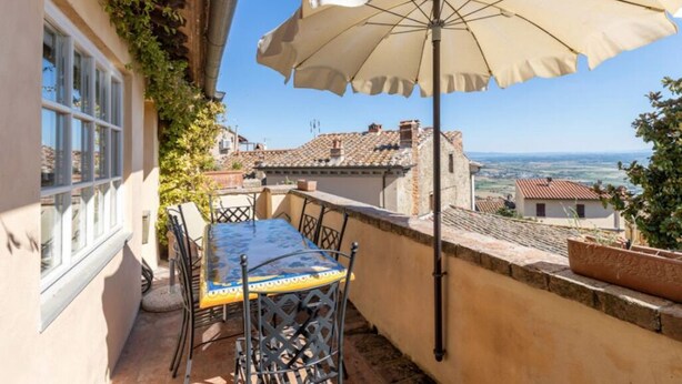 A terrace with a table and chairs, an umbrella, and a view of the countryside.