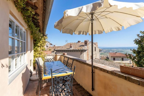 Um terraço com mesa, cadeiras, um guarda-sol e vista para o campo.