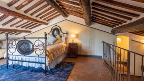 A bedroom with a wooden ceiling, a bed with a metal frame, a nightstand, and a staircase with a railing.