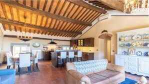 A spacious living area with a high wooden ceiling, a dining table with chairs, a sofa, and a kitchen area with bar stools.