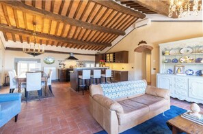 Ampla sala de estar com teto alto de madeira, mesa de jantar com cadeiras, sofá e área de cozinha com banquetas.