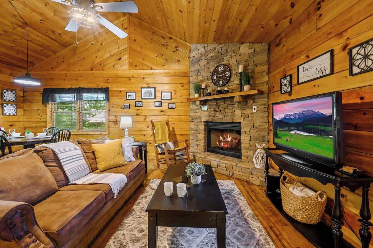 A cozy cabin interior with a wooden interior, a fireplace, a television, and a dining area.