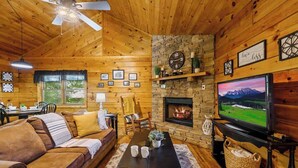 Un intérieur de chalet chaleureux, avec un décor en bois, une cheminée, un téléviseur et un coin repas.