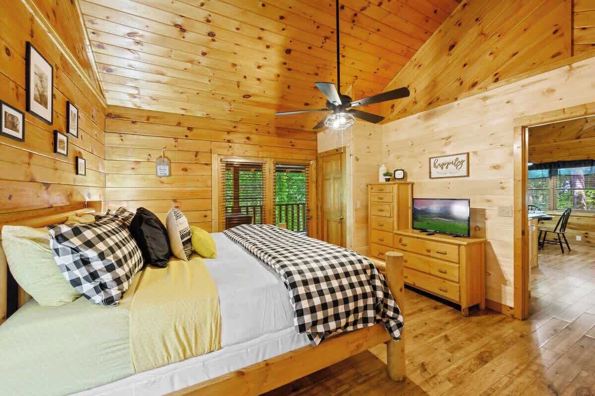 A wooden cabin room with a bed, a television, and a ceiling fan.