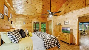 Une chambre dans un chalet en bois, équipée d’un lit, d’une télévision et d’un ventilateur de plafond.