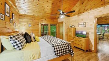 A wooden cabin room with a bed, a television, and a ceiling fan.