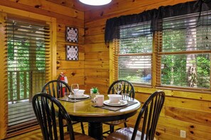 A wooden cabin interior with a dining table set for four, surrounded by chairs. - Location! Log Cabin,Hot Tub,Fireplace,Pool,Fishing! (Sevierville)