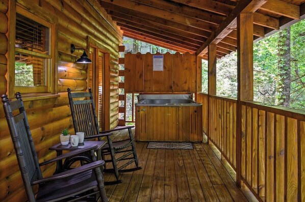 A wooden cabin with a porch, a hot tub, and a table with chairs. - Location! Log Cabin,Hot Tub,Fireplace,Pool,Fishing! (Sevierville)