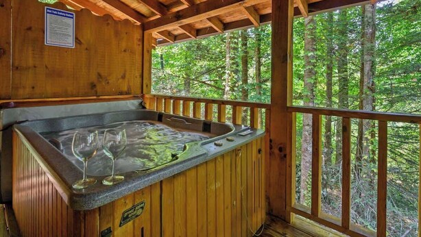 Une cabane en bois dotée d’un bain à remous, d’une terrasse en bois et offrant une vue sur une forêt.