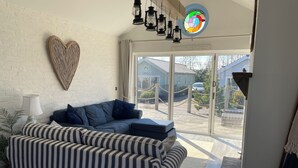 A modern living room with a striped sofa, a heart-shaped wall decoration, and a view through large glass doors.