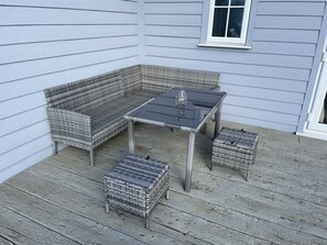 A covered patio with wicker furniture, including a sofa, table, and ottoman, against a light blue house exterior. - Beach House Paradise Found WF-Fi, Netflix, Pool,Gym, Pet Friendly close to beach (Filey)