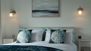 A neatly arranged bedroom with a bed, pillows, a painting, and two wall-mounted lights.