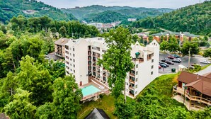 A multi-story hotel with a swimming pool, surrounded by lush greenery and hills.