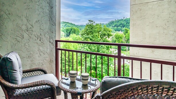 A balcony with wicker furniture and a table with two cups, overlooking a green landscape.