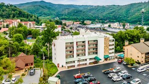 A multi-story hotel with a parking lot, surrounded by greenery and hills.