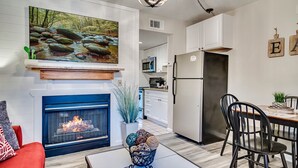 A modern kitchen with white cabinets, a stainless steel refrigerator, and a dining area with black chairs.