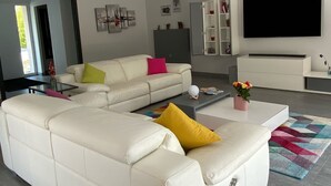Moderni olohuone, jossa on kulmasohva, litteänäyttöinen televisio ja lasinen sohvapöytä.