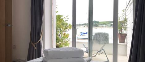 A hotel room with a bed, a window with curtains, a view of the sea, and a potted plant on the windowsill.