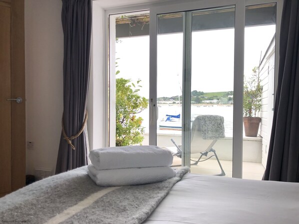 A hotel room with a bed, a window with curtains, a view of the sea, and a potted plant on the windowsill.