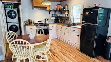 A kitchen with wooden flooring, a dining table with chairs, a refrigerator, a stove, and a washing machine.