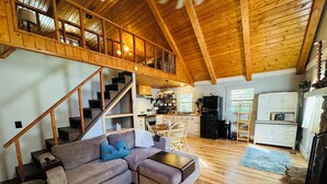 A spacious living area with a wooden staircase, a kitchen, and a dining area. - Waterfront Cabin on trophy trout stream, fire pit, smart tv, fireplace (Ellijay)