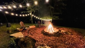 An outdoor seating area with Adirondack chairs, a fire pit, and string lights. - Waterfront Cabin on trophy trout stream, fire pit, smart tv, fireplace (Ellijay)