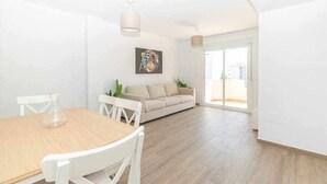 Un vaste espace de vie comprenant une table à manger, des chaises blanches, un canapé beige et une grande fenêtre.