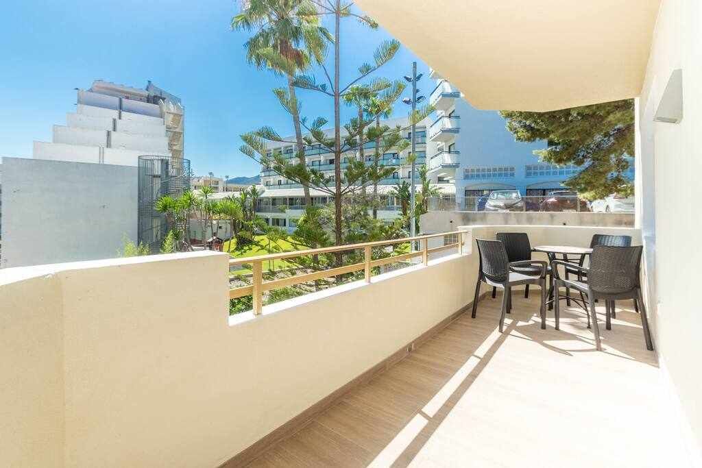 A balcony with a table and chairs, overlooking a cityscape with modern buildings and trees.