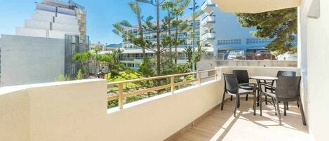 A balcony with a table and chairs, overlooking a cityscape with modern buildings and trees.