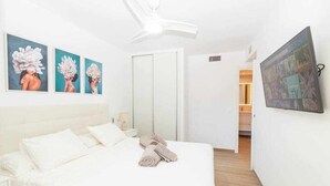 Une chambre d’hôtel avec un lit, un ventilateur de plafond, une télévision et des œuvres d’art accrochées au mur.