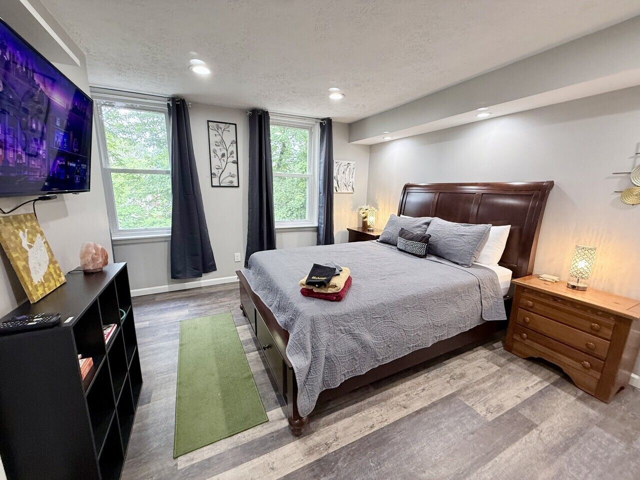 Een slaapkamer met een bed, nachtkastjes, een televisie, een boekenkast en een raam met gordijnen.