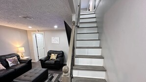 Ein modernes Wohnzimmer mit Treppe, Ledersofas und einem gemusterten Teppich.