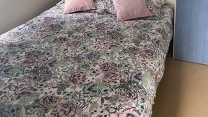 A bedroom with a bed, two pillows, a shelf above the bed, and a window with curtains.