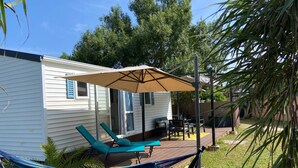 Een klein huis met een patio, voorzien van een hangmat, twee lounge fauteuils en een grote parasol.
