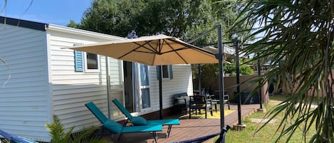 A small house with a patio area featuring a hammock, two lounge chairs, and a large umbrella.