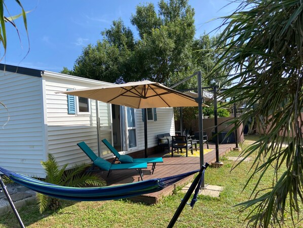 A small house with a patio area featuring a hammock, two lounge chairs, and a large umbrella.