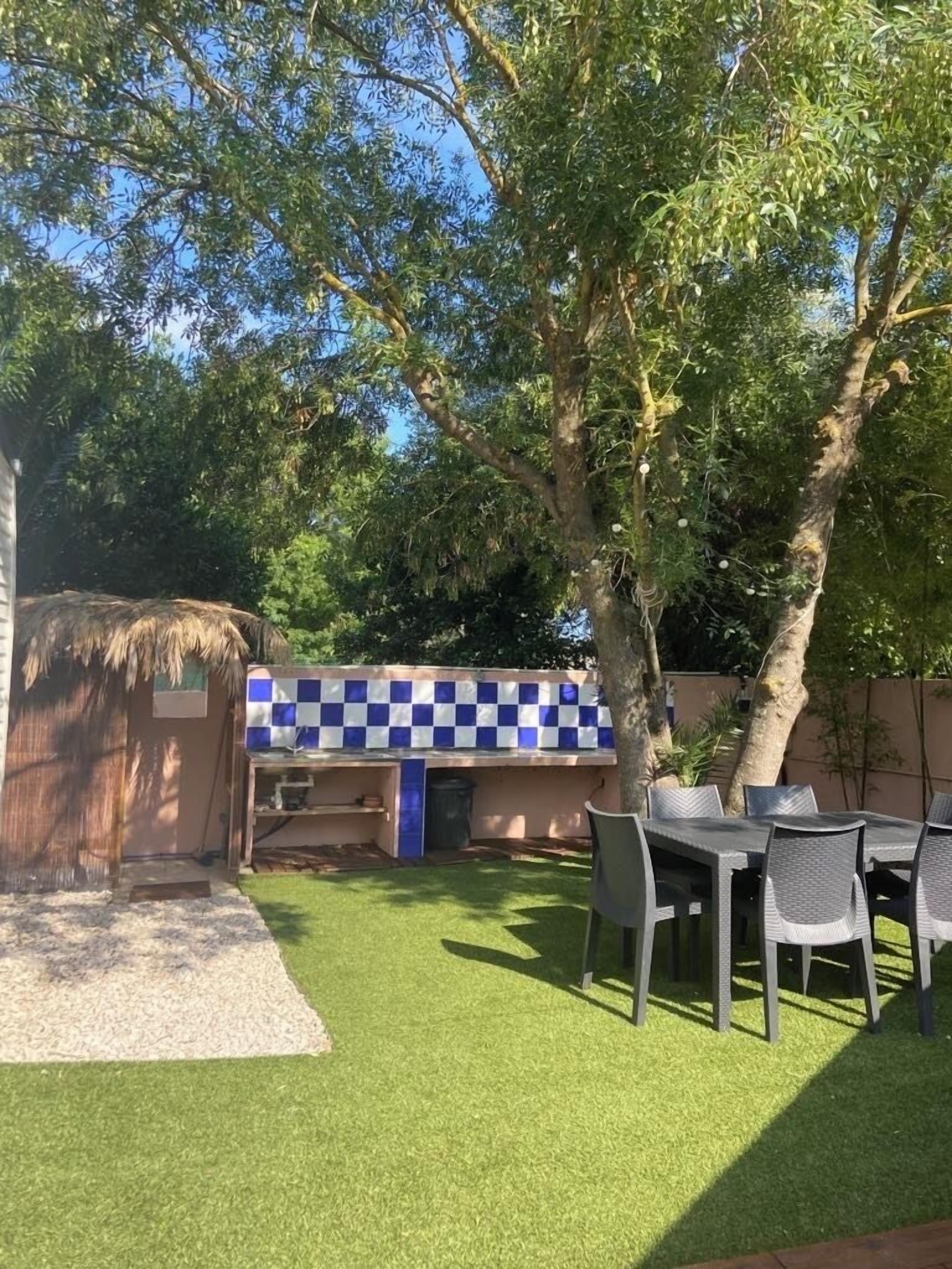 A backyard with artificial grass, a table with chairs, and a blue and white checkered wall.