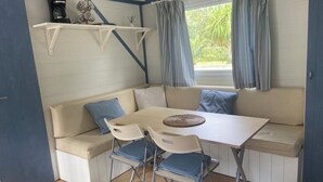 A compact living space with a sofa, a small table, and two chairs. There are shelves above the sofa and a window with curtains.