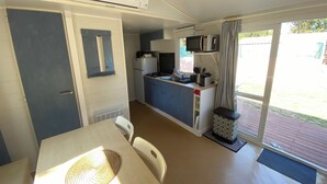 A compact kitchen with a microwave, stove, and sink, a dining table with chairs, and a sliding glass door to the outside.