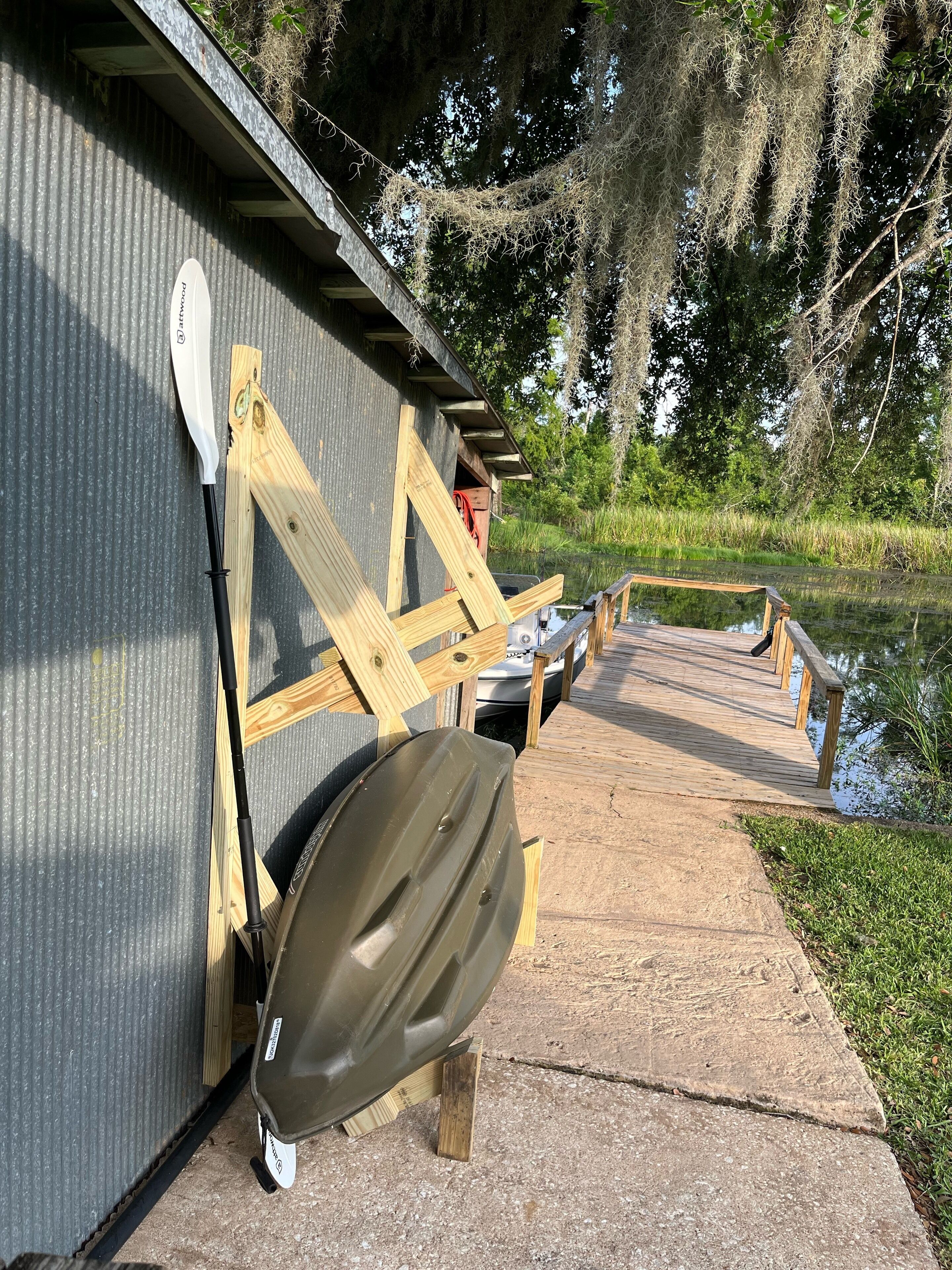 A wooden dock leading to a building with a kayak and paddleboard leaning against it.
