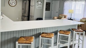 Une cuisine moderne avec un îlot central, des tabourets de bar, une horloge et un panneau décoratif sur le mur avec le mot « merci ».