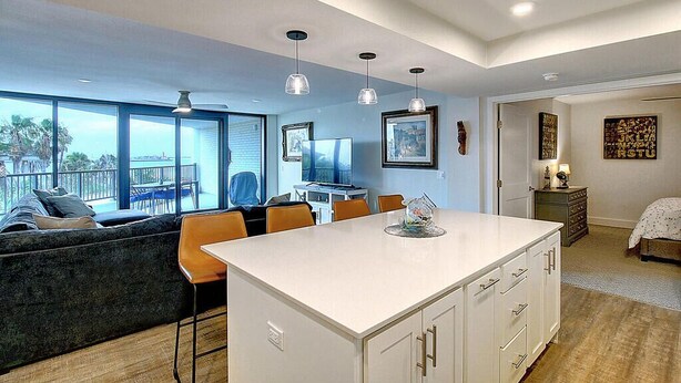 Una cocina moderna con una isla central, un comedor con sillas, un sofá y vistas al exterior.