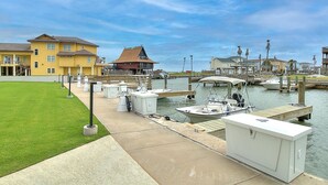 Un puerto deportivo con barcos amarrados, una zona verde y edificios al fondo.