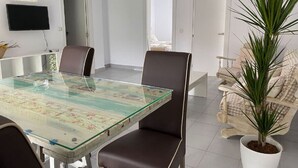 Un soggiorno moderno con un tavolo da pranzo in vetro, poltrone in pelle scura, una pianta in vaso bianca e un televisore fissato alla parete.